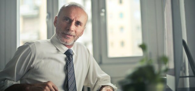 older adult in suit at desk