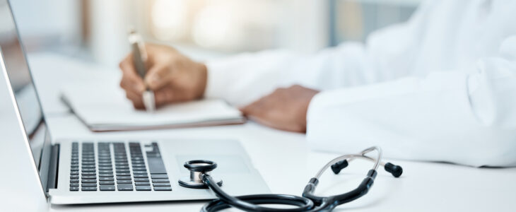 Laptop, stethoscope and doctor writing in notebook for research planning or medical tech innovation in hospital office. Healthcare medic worker, research strategy book notes and online communication